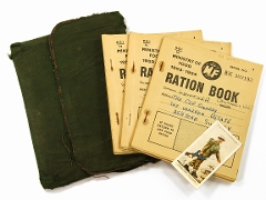 Three fawn coloured booklets with printing and handwriting. Dark green fabric wallet. Rectangular card with picture of an infantry soldier from 1939 holding a rifle. To magnify click now