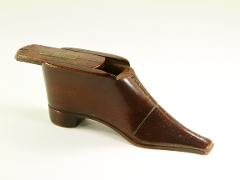 Dark wooden box in the shape of a narrow shoe with heel and long toe, facing right. Sliding lid on top, half open to reveal void. Pattern on toe and to mimic laces. To magnify click now