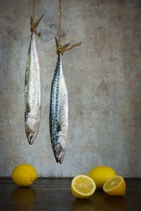 two fish hanging by their tails facing a surface with 3 lemons on it. 1 lemon is cut in half.