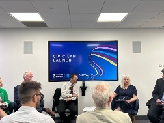 Five adults sitting at the front of a room at a panel events. Two women and three men.